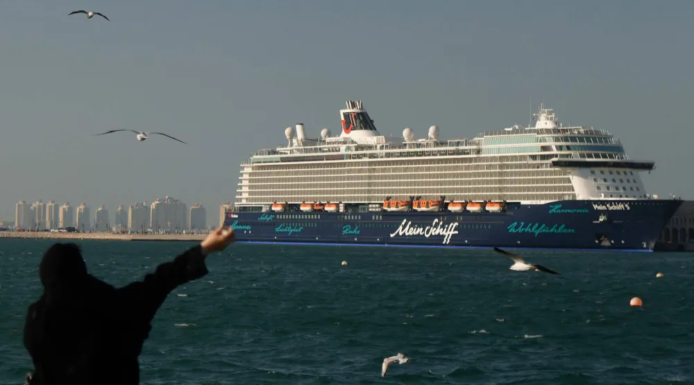 امرأة تطعم طيور النورس على طول الممشى البحري وخلفها سفينة الرحلات البحرية «ماين شيف» الراسية في منطقة ميناء الدوحة (أ.ف.ب)