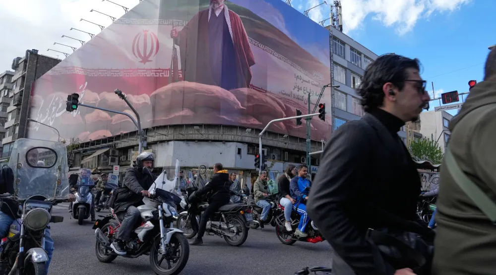 أشخاص يقودون دراجاتهم النارية أمام لوحة إعلانية تعرض صورة للمرشد الجديد مجتبى خامنئي في وسط طهران (أ.ب)