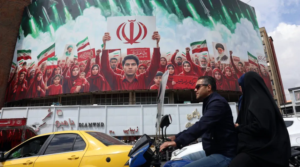 إيرانيون يمرون بسياراتهم أمام لوحة إعلانات سياسية تعرض أعلام إيران في إحدى ساحات العاصمة طهران 6 أبريل 2026 (إ.ب.أ)