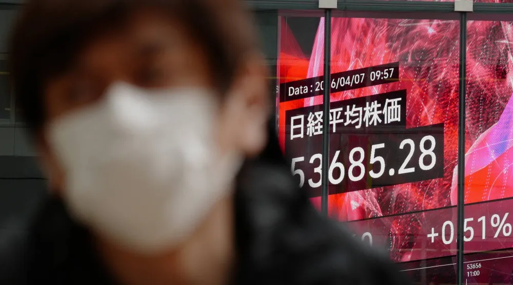 شخص يسير أمام لوحة إلكترونية تعرض مؤشر «نيكي» الياباني في طوكيو (أ.ب)