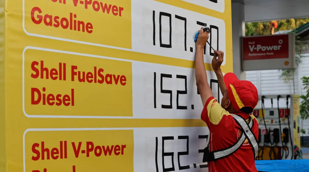 عامل يستخدم شريطاً لاصقاً لتغيير أرقام أسعار الوقود في محطة وقود بمدينة كويزون، مترو مانيلا (إ.ب.أ)