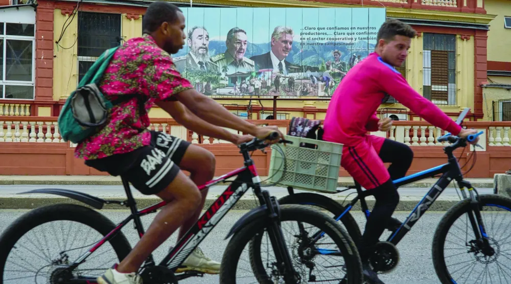 درّاجان يمرّان بجدارية للزعيم الكوبي الراحل فيديل كاسترو وخلفه راؤول كاسترو والرئيس الحالي ميغيل دياز كانل وسط هافانا (أ.ب)