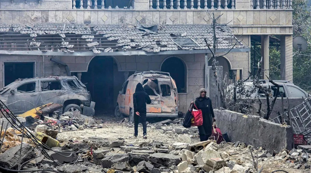 امرأة تسير حاملة ما أمكن إنقاذه من مقتنياتها بين أنقاض مبنى دمّرته غارات إسرائيلية ليلية على بلدة معركة في جنوب لبنان (أ.ف.ب)