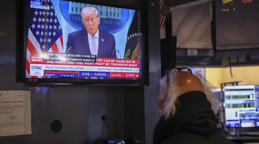 متداول يراقب شاشة تُظهر الرئيس دونالد ترمب يتحدث خلال مؤتمر صحافي حول الحرب مع إيران في بورصة نيويورك (إ.ب.أ)