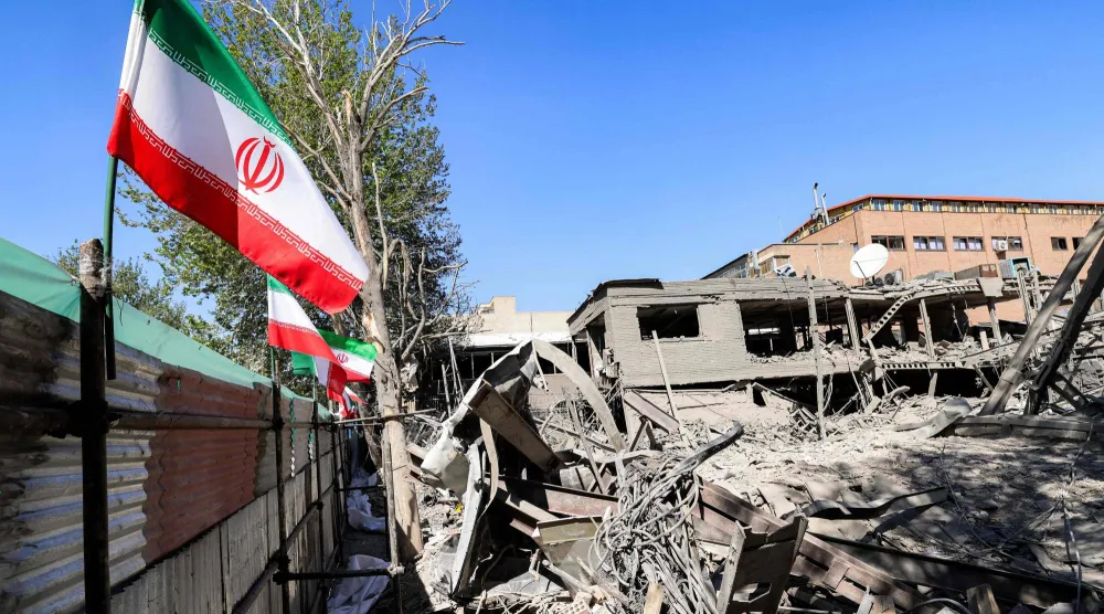 العلم الإيراني يظهر بجوار أنقاض مبنى منهار عقب الهجمات التي استهدفت جامعة في طهران (أ.ف.ب)