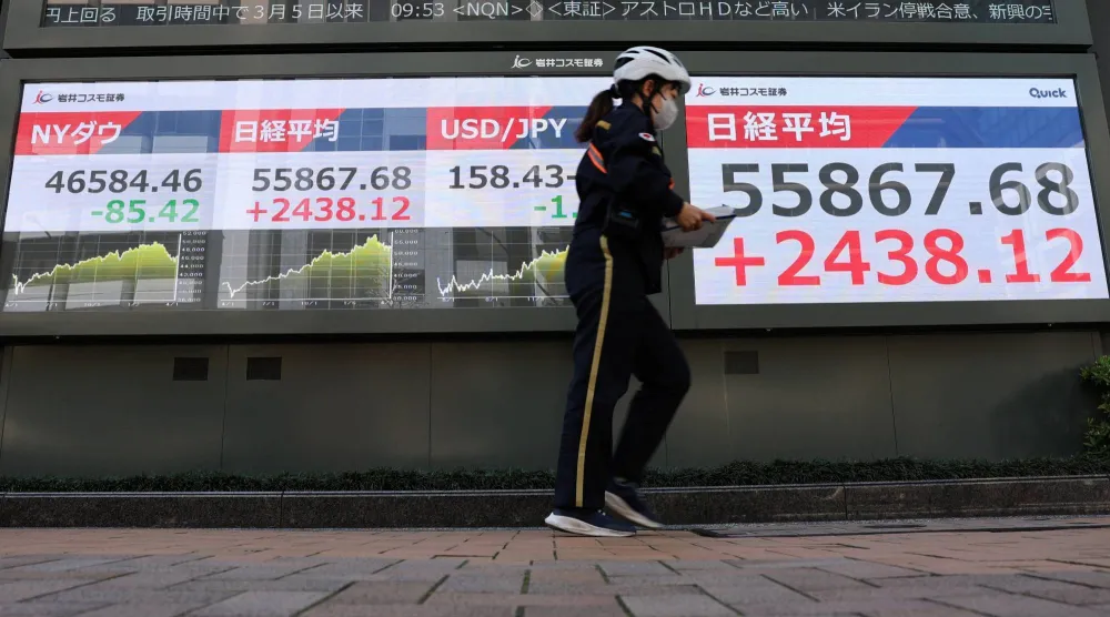 ساعية بريد تمر أمام شاشة تعرض حركة الأسهم في طوكيو (رويترز)