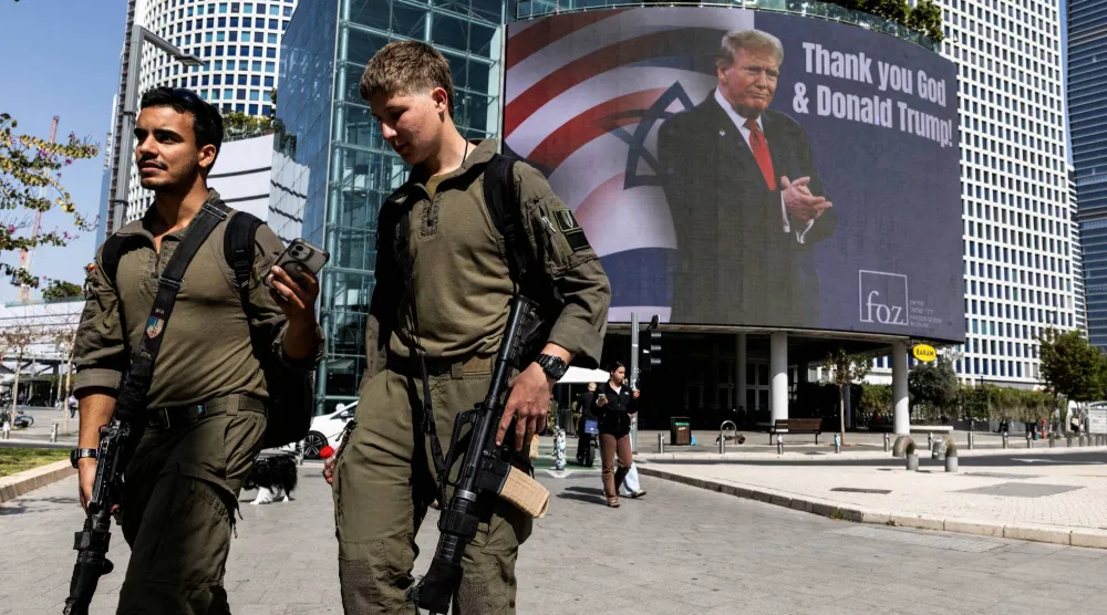 جنود إسرائيليون يمرون بجوار لوحة إعلانية تعرض صورة الرئيس الأميركي دونالد ترمب في تل أبيب (رويترز)