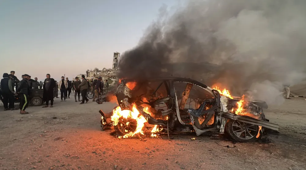 يقف الناس قرب سيارة محترقة عقب غارة إسرائيلية أسفرت عن مقتل في قناة الجزيرة (د.ب.أ)