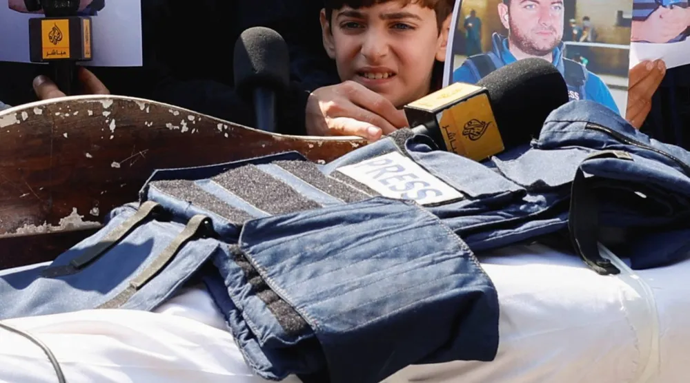 ينظر ابن الصحافي محمد وشاح نحو سترة وميكروفون موضوعين على جثمان والده خلال جنازته في مستشفى شهداء الأقصى بدير البلح (رويترز)