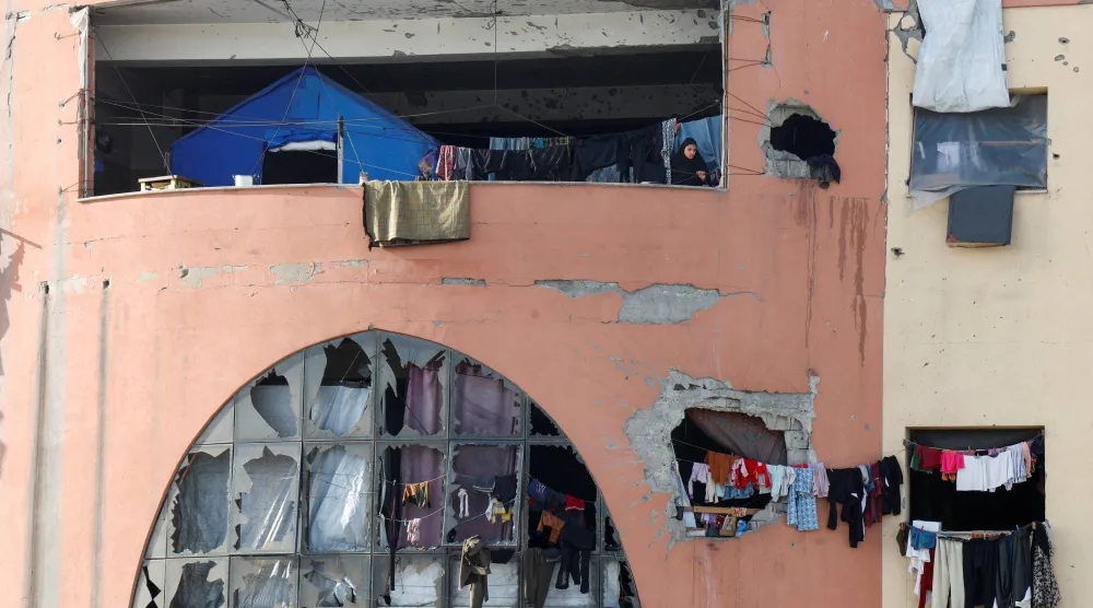 امرأة فلسطينية نازحة تقف على شرفة داخل مبنى مهدم في جامعة الأقصى جنوب غزة يُستخدم كمأوى (رويترز)