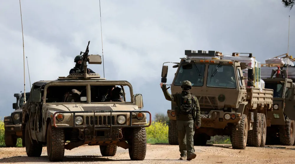 جندي إسرائيلي يشير بيده أثناء سيره بجوار مركبات عسكرية بالقرب من الحدود مع لبنان... شمال إسرائيل 30 مارس 2026 (رويترز)
