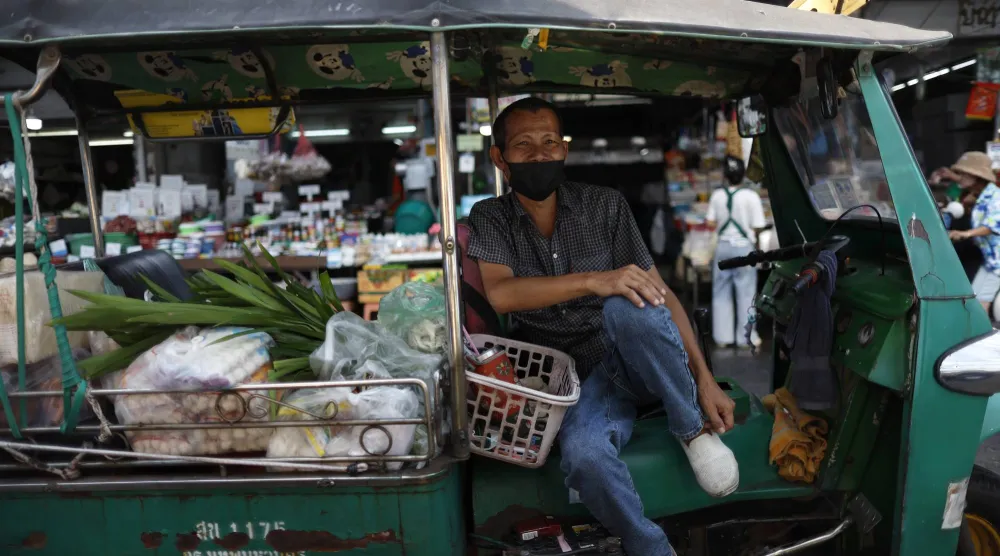 سائق توك توك وهي مركبة أجرة ثلاثية العجلات ينتظر ركاباً يشترون الطعام في سوق ببانكوك (إ.ب.أ)