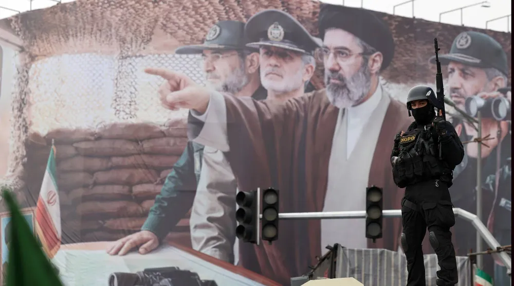 جندي إيراني يقف أمام لوحة دعائية في طهران وتظهر المرشد الجديد مجتبى خامنئي وقادة عسكريين بينهم علي رضا تنغسيري قائد بحرية «الحرس الثوري» قبل مقتله في بندر عباس (إ.ب.أ)