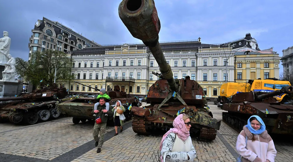 سكان يحملون سلالهم المليئة بالكعك والبيض التقليديين في أثناء مرورهم بمعرض للمعدات العسكرية الروسية المدمرة خلال احتفالات عيد الفصح في كييف الأحد (أ.ف.ب)