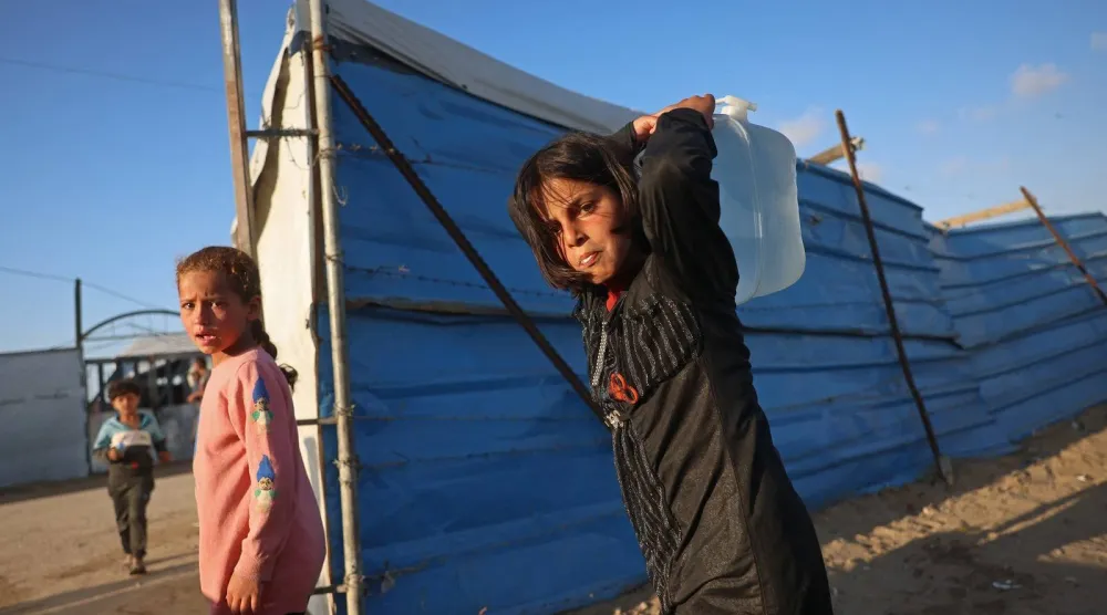 فتاة فلسطينية تحمل وعاء ماء في مخيم للنازحين بخان يونس جنوب غزة (أ.ف.ب)