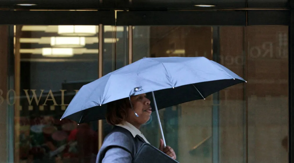 امرأة تسير تحت المطر في شارع «وول ستريت» بنيويورك (رويترز)