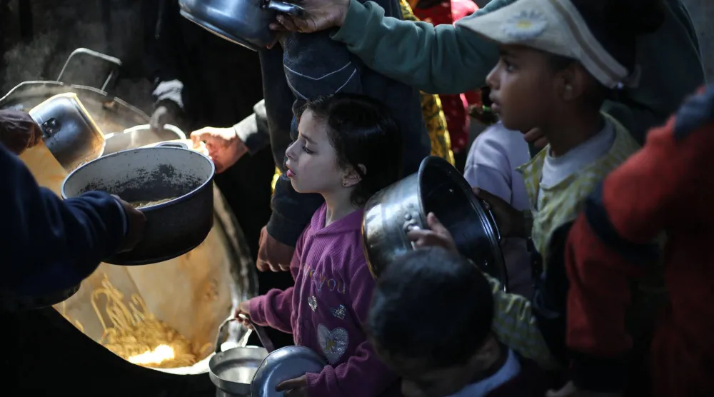 أطفال فلسطينيون نازحون يتلقون الطعام من مطبخ خيري في مخيم النصيرات للاجئين وسط غزة يوم الاثنين (أ.ف.ب)