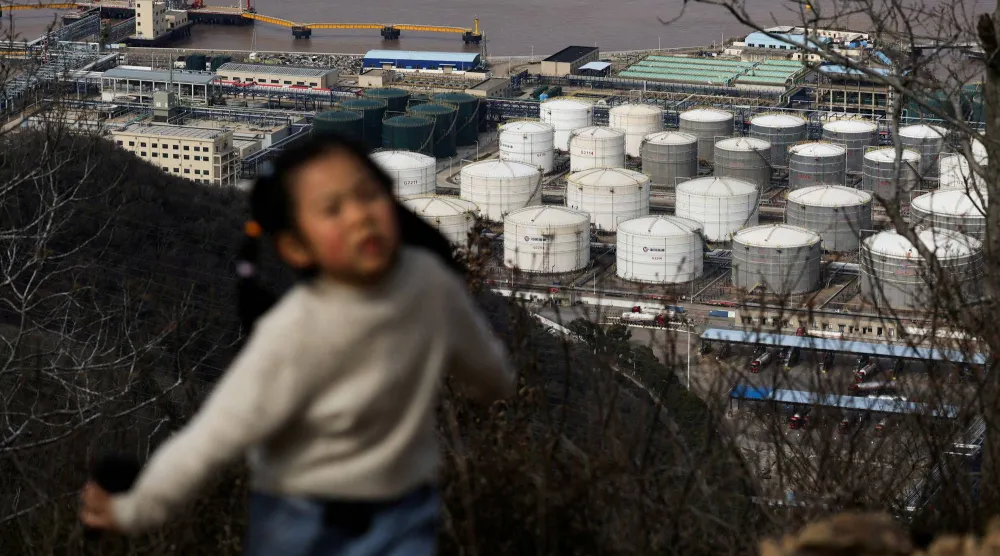 طفل يسير على طول ممر للمشي وخلفه خزانات تخزين نفط في نينغبو، الصين (رويترز)