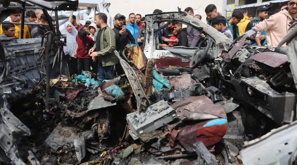 فلسطينيون يتجمعون حول حطام سيارة الشرطة التي دُمرت في الغارة الإسرائيلية (أ.ف.ب)
