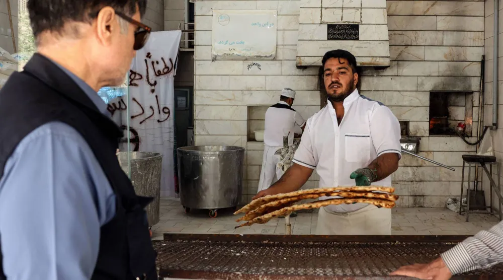 عامل يقدم الخبز للزبائن في مخبز جنوب طهران (أ.ف.ب)