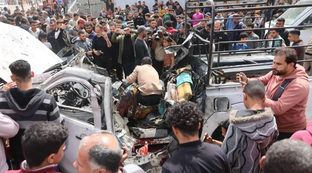 فلسطينيون في موقع حطام سيارة شرطة دمرتها غارة إسرائيلية في مدينة غزة يوم الثلاثاء (أ.ف.ب)