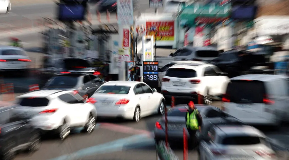 لوحة تعرض أسعار النفط بينما تنتظر السيارات في طابور عند محطة وقود في سيول (رويترز)