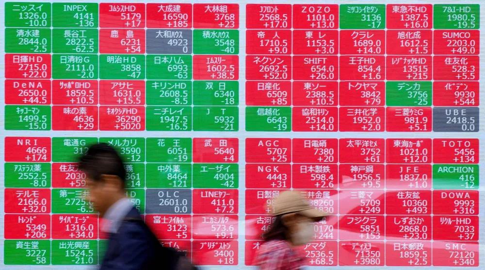 مشاة يمرون أمام شاشة تعرض حركة الأسهم في وسط العاصمة اليابانية طوكيو (أ.ف.ب)