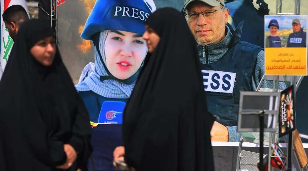 أشخاص يمرون أمام لافتة تعرض صور الصحافييَن فاطمة فتوني وعلي شعيب اللذين قُتلا في غارة إسرائيلية في جنوب لبنان خلال مظاهرة في بغداد 7 أبريل 2026 (أ.ف.ب)