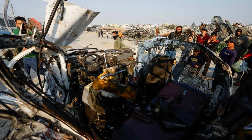 فلسطينيون وسط غزة يفحصون موقع غارة إسرائيلية استهدفت سيارة شرطة (رويترز)