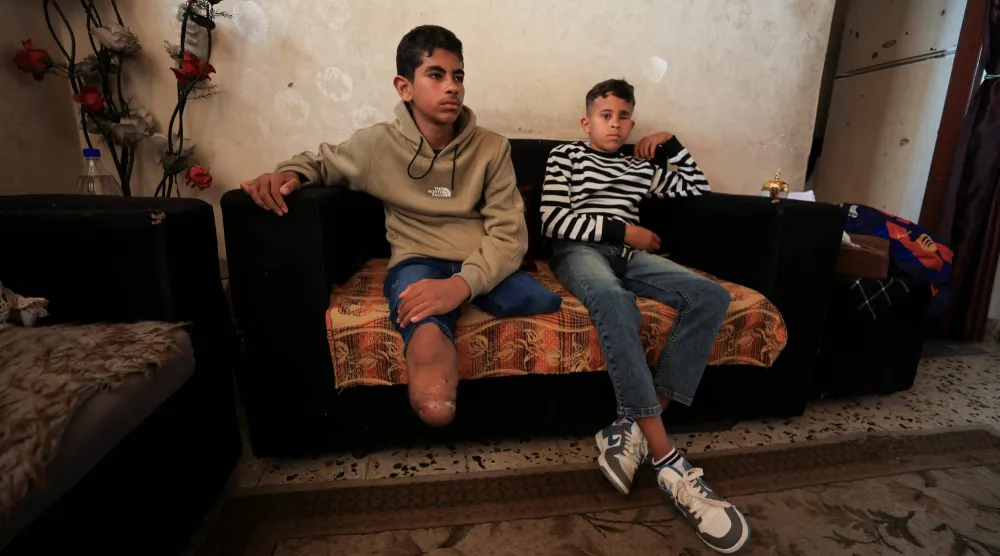 يجلس فاضل الناجي البالغ 14 عاماً الذي فقد ساقيه بجانب شقيقه أمير صاحب الـ11 عاماً الذي فقد إحدى عينيه بعد إصابتهما خلال غارة إسرائيلية في منزلهما بمدينة غزة (رويترز)