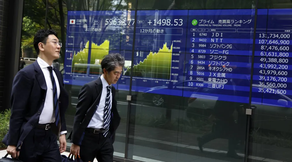 رجلان يمران أمام شاشة تعرض حركة الأسهم والعملات في العاصمة اليابانية طوكيو (إ.ب.أ)