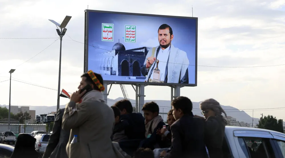 أشخاص يستقلون سيارة في صنعاء تمر أمام لوحة إعلانية رقمية تحمل صورة زعيم الحوثيين يوم 9 أبريل 2026 (إ.ب.أ)