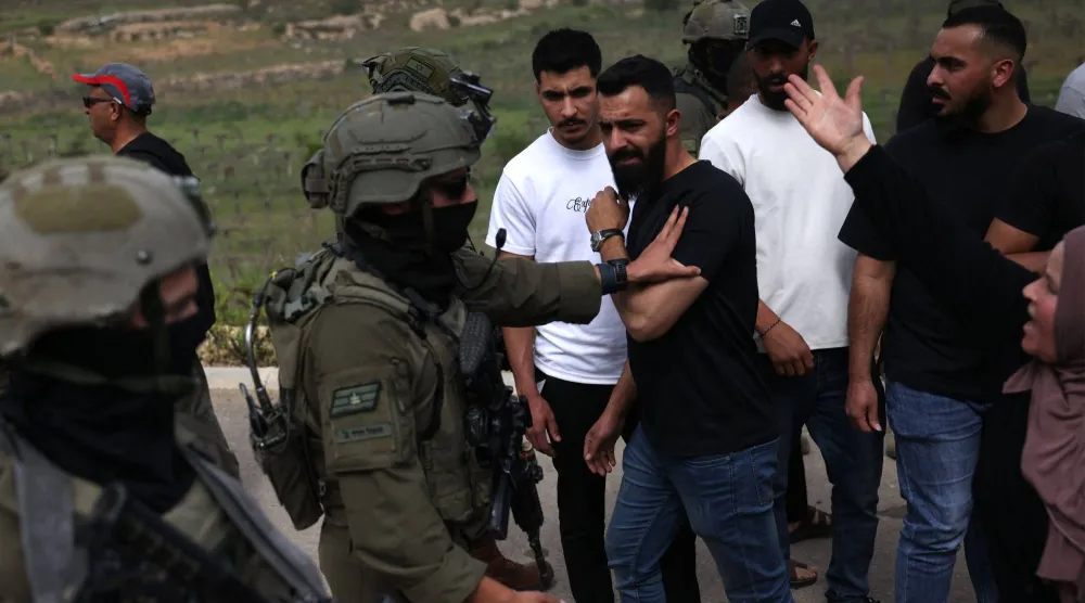 جندي إسرائيلي يدفع رجلاً أثناء إجلاء فلسطينيين قسراً من أراضيهم بعد أن هاجم مستوطنون إسرائيليون مزارعين محليين أمس قرب قرية حلحول الفلسطينية جنوب مدينة الخليل في الضفة الغربية المحتلة (أ.ف.ب)