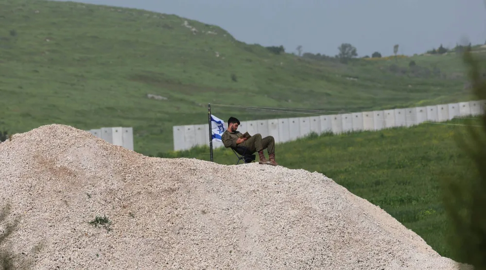 جندي إسرائيلي بجوار العلم الإسرائيلي قرب الحاجز الأمني ​​بين إسرائيل ولبنان بالقرب من أفيفيم شمال إسرائيل (إ.ب.أ)