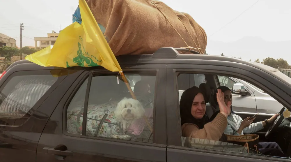 عائلة نازحة خلال عودتها إلى قريتها في الجنوب إثر الإعلان عن الهدنة وهي ترفع علم «حزب الله» على السيارة (رويترز)