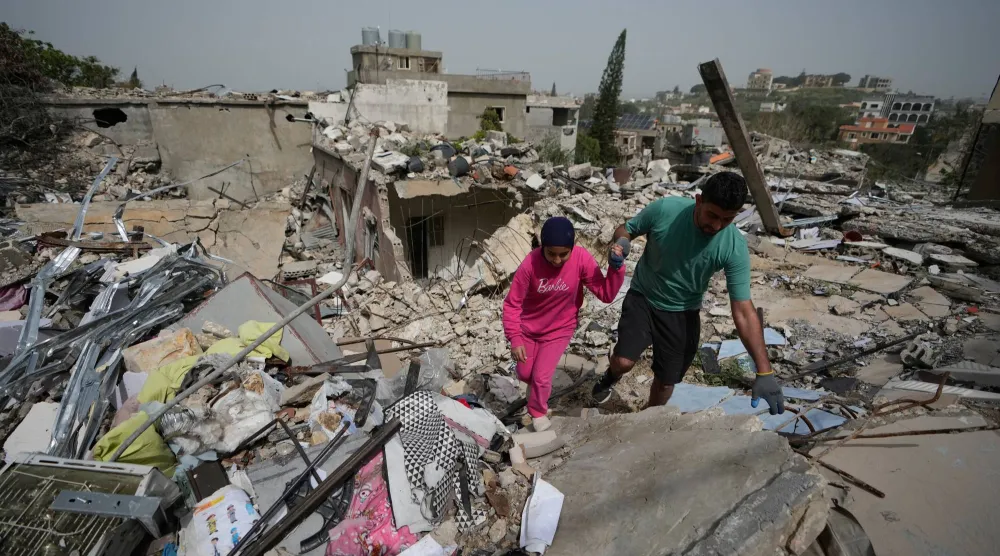 مواطنون يمشون على أنقاض منزل مُدمَّر نتيجة القصف الإسرائيلي في بلدة جبشيت بجنوب لبنان (أ.ب)