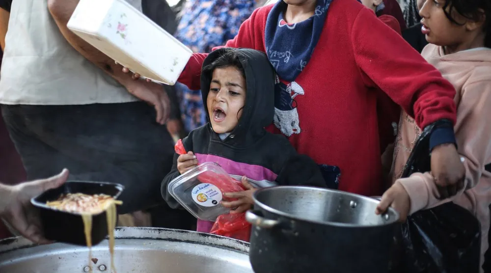 أطفال فلسطينيون نازحون يتلقون الطعام من مطبخ خيري في مخيم النصيرات للاجئين (أ.ف.ب) 