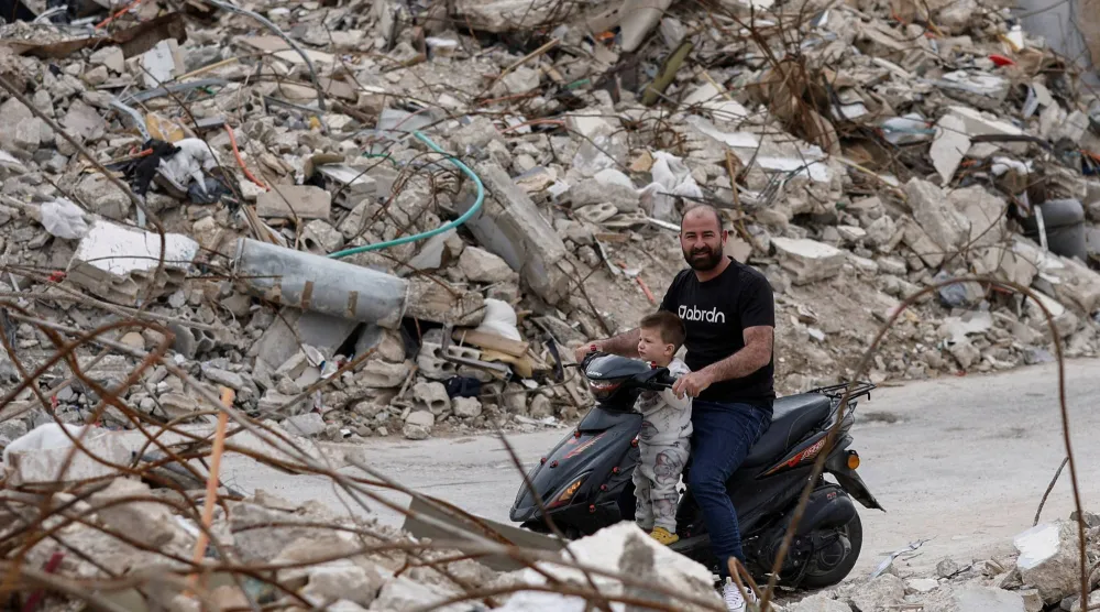 رجل وطفله ينظران إلى أنقاض المنازل التي دمرتها الغارات الإسرائيلية في جنوب لبنان (رويترز)