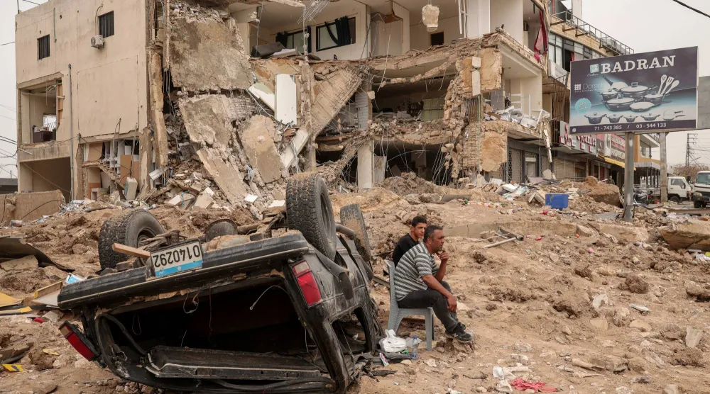 شخصان يجلسان أمس وسط خراب في صور تسببت به ضربة إسرائيلية قبيل سريان هدنة الـ 10  أيام  (رويترز)