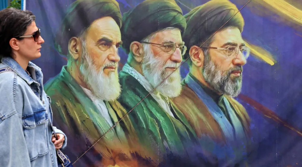 إيرانية تمر أمام لافتة تظهر عليها صورتا المرشدين الأول والثاني الخميني (يسار) وعلي خامنئي (وسط) بجانب المرشد الجديد مجتبى خامنئي في طهران الأحد (أ.ف.ب)
