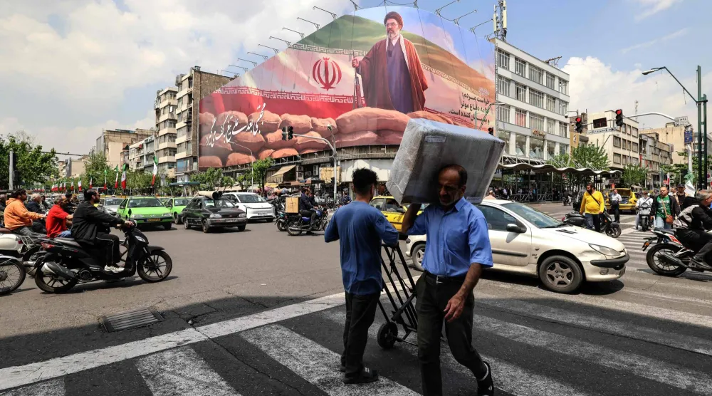 رجل يحمل طرداً على كتفه يمر أمام لوحة إعلانية كبيرة تصور المرشد مجتبى خامنئي في أحد شوارع طهران الاثنين (أ.ف.ب)