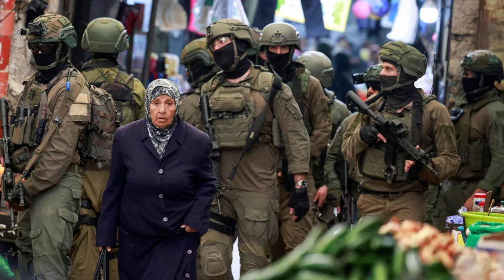 امرأة فلسطينية تمر بجوار جنود إسرائيليين يقومون بدورية في سوق البلدة القديمة بمدينة نابلس شمال الضفة الغربية المحتلة (أ.ف.ب)