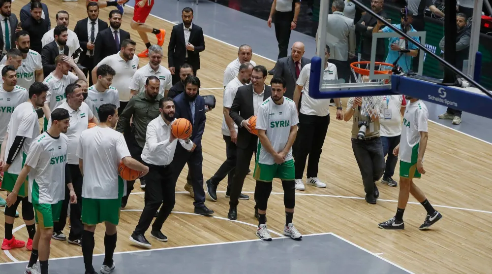 الرئيس السوري أحمد الشرع (وسط الصورة إلى اليسار) يسدد رمية حرة قبل مباراة ودية بين المنتخبين السوري واللبناني في حفل إعادة افتتاح صالة الفيحاء لكرة السلة بدمشق (أ.ب)