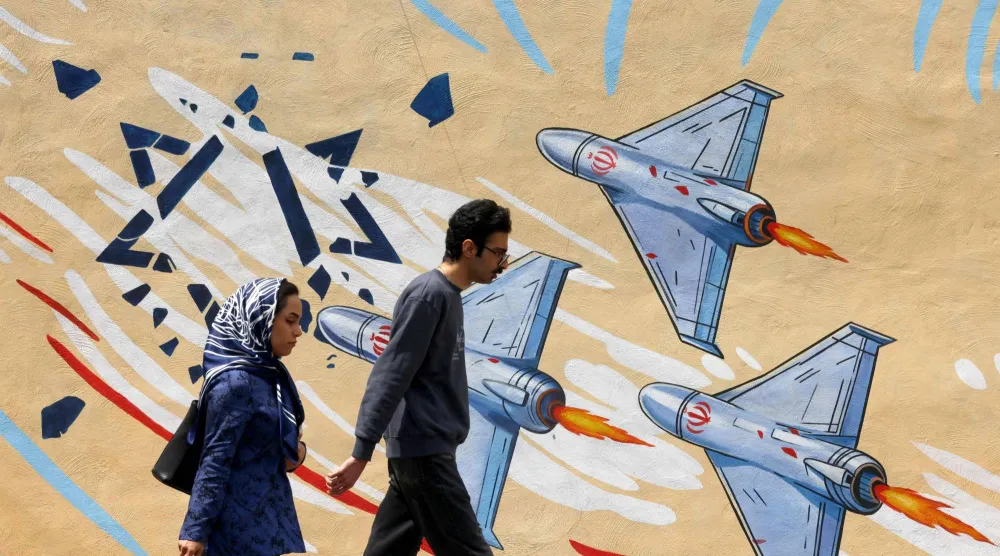 إيرانيان يمران أمام لوحة جدارية مناهضة للولايات المتحدة وإسرائيل في طهران (أ.ف.ب)