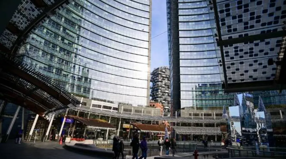 عابرو سبيل يسيرون عبر ساحة عامة في منطقة الأعمال بورتا نوفا محاطين بمباني مكاتب حديثة في ميلانو (رويترز)