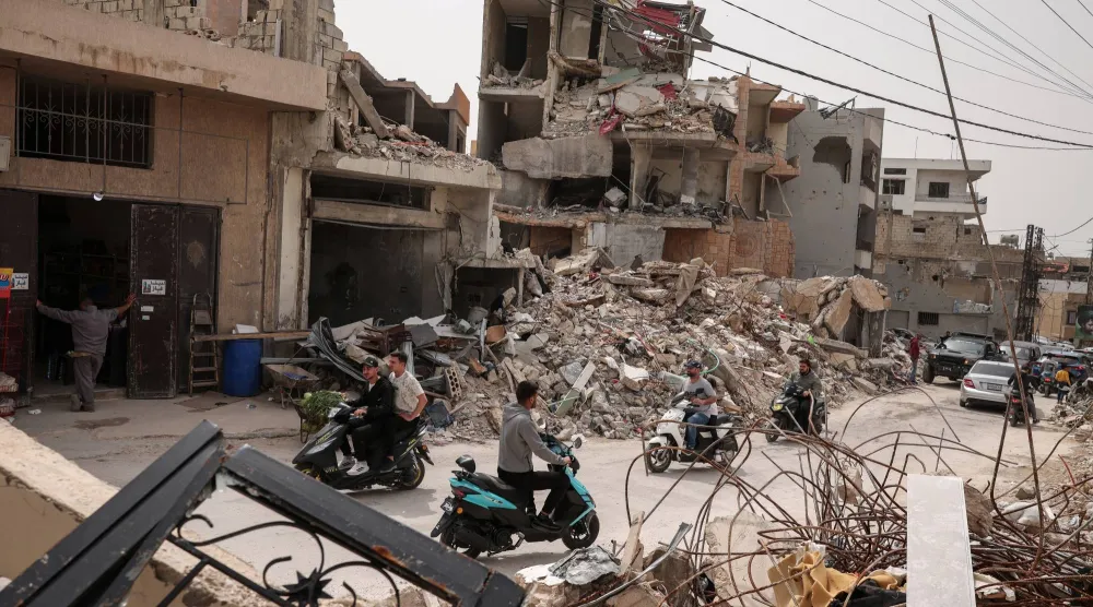 أشخاص يسيرون بجوار أنقاض المنازل التي دمرتها الغارات الإسرائيلية في طير دبا بجنوب لبنان (رويترز)