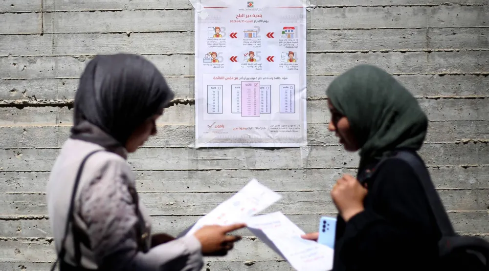 سيدتان فلسطينيتان تقرآن تعليمات التصويت بالانتخابات المحلية في مدينة دير البلح بوسط غزة يوم الثلاثاء (أ.ف.ب)