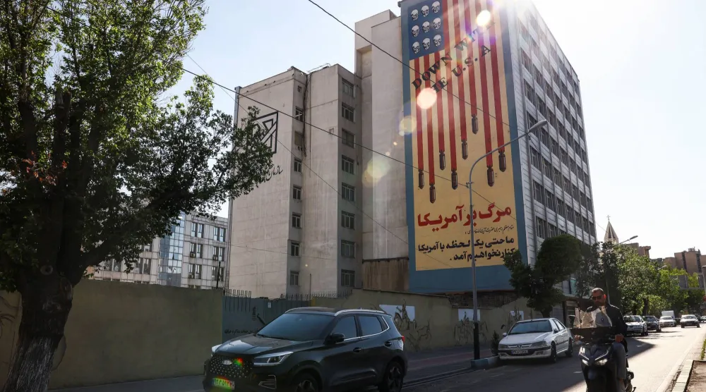 رجل يمر على دراجة نارية أمام جدارية مناهضة للولايات المتحدة على أحد المباني في طهران (رويترز)