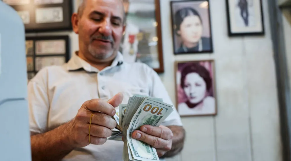 عامل يعدّ أوراقاً نقدية من فئة الدولار داخل محل صرافة ببغداد (أ.ف.ب)