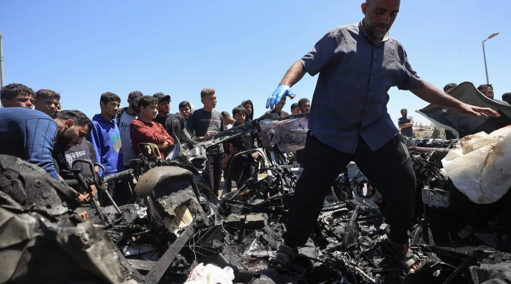 فلسطينيون في موقع استهداف سيارة بغارة جوية إسرائيلية في شارع صلاح الدين جنوب مخيم البريج وسط غزة الخميس (أ.ف.ب)